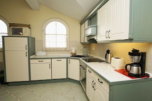 A kitchen with white cabinets, a window with lace curtains, a microwave, a toaster, and a coffee maker. - Right behind the dune, with a balcony and a view of the sea - Strandvilla Böck FeWo 15 - (Glowe)