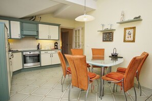 A compact kitchen with a dining area, featuring a round glass table and orange chairs. - Right behind the dune, with a balcony and a view of the sea - Strandvilla Böck FeWo 15 - (Glowe)