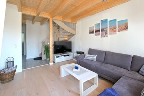 A modern living room with a grey sofa, a white coffee table, a flat-screen TV, and a staircase leading to another level. - Fhaus MantjeMantje - Holiday home with sea view, terrace and private sauna - (Gager)