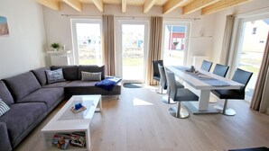 A modern living room with a sofa, a coffee table, a dining table with chairs, and large windows.