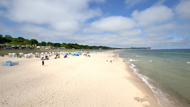 A wide sandy beach with tents and people, a clear sky, and a calm sea.