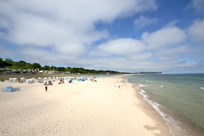 A wide sandy beach with tents and people, a clear sky, and a calm sea.