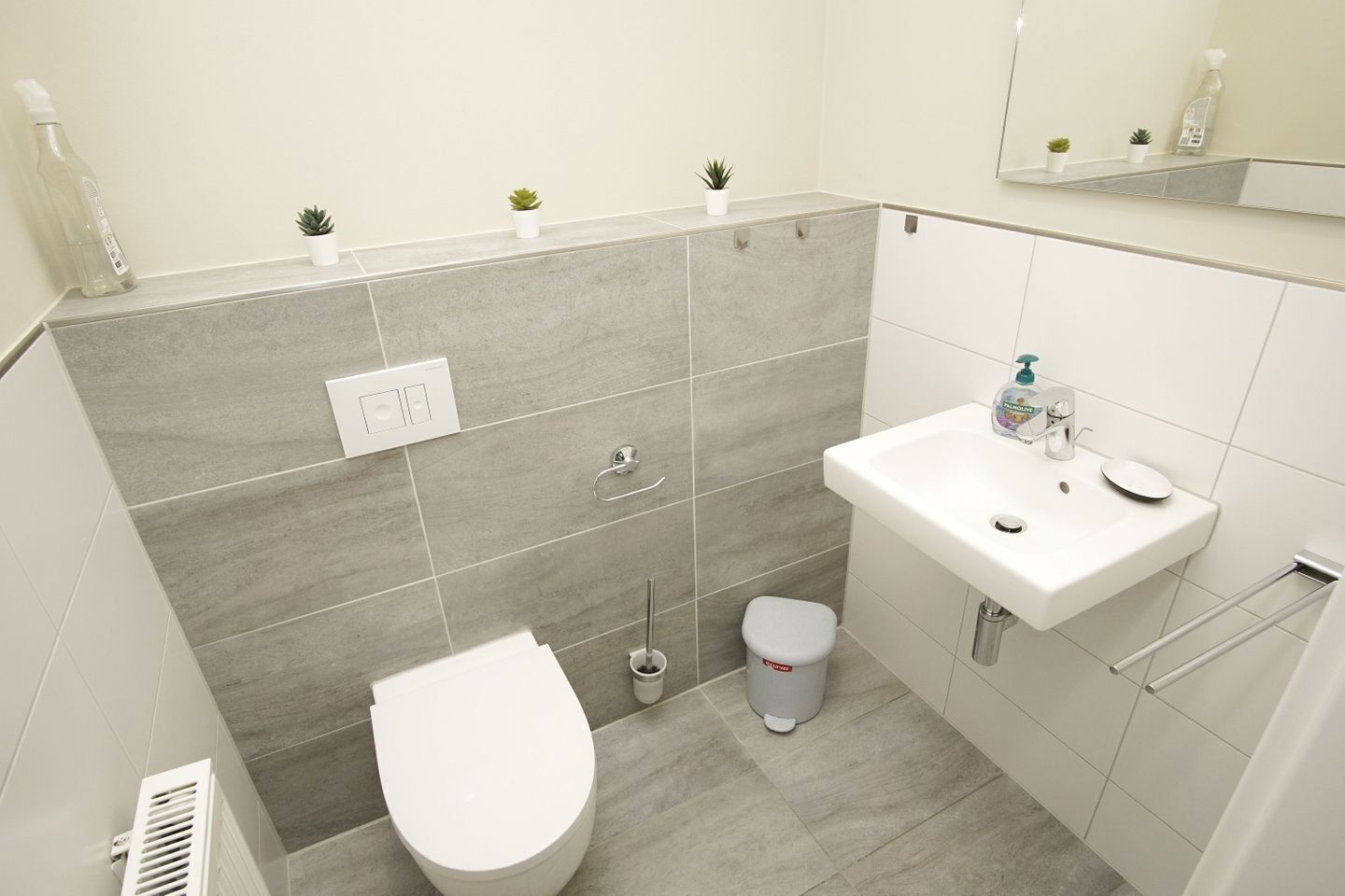 A modern bathroom with a toilet, sink, and small potted plants on the wall.