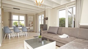 Un salon moderne avec un canapé, une table basse et des fauteuils. On y trouve une cheminée, une bibliothèque et un coin repas avec une table et des chaises.