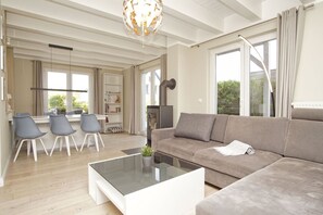 A modern living room with a sofa, coffee table, and chairs. There is a fireplace, a bookshelf, and a dining area with a table and chairs.