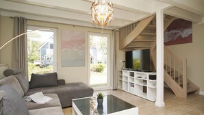 Un salon avec un canapé gris, une table basse en verre, un téléviseur posé sur un meuble blanc, et un escalier doté d’une rampe en bois.