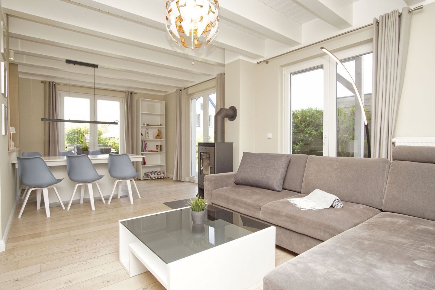 A modern living room with a sofa, coffee table, and chairs. There is a fireplace, a bookshelf, and a dining area with a table and chairs.