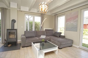 A modern living room with a grey sofa, a glass coffee table, a wood-burning stove, and large windows.