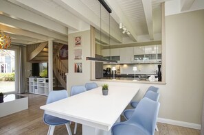 A modern kitchen with white cabinets, a large island, and a dining area with a white table and blue chairs.