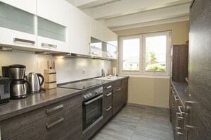 Una cocina moderna con encimera de madera oscura, electrodomésticos de acero inoxidable y un ventanal que deja entrar luz natural.