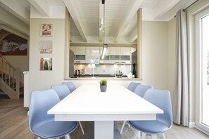 Ein moderner Essbereich mit einem weißen Tisch und blauen Stühlen, eine Küche mit weißen Schränken und eine Treppe zu einer anderen Ebene.