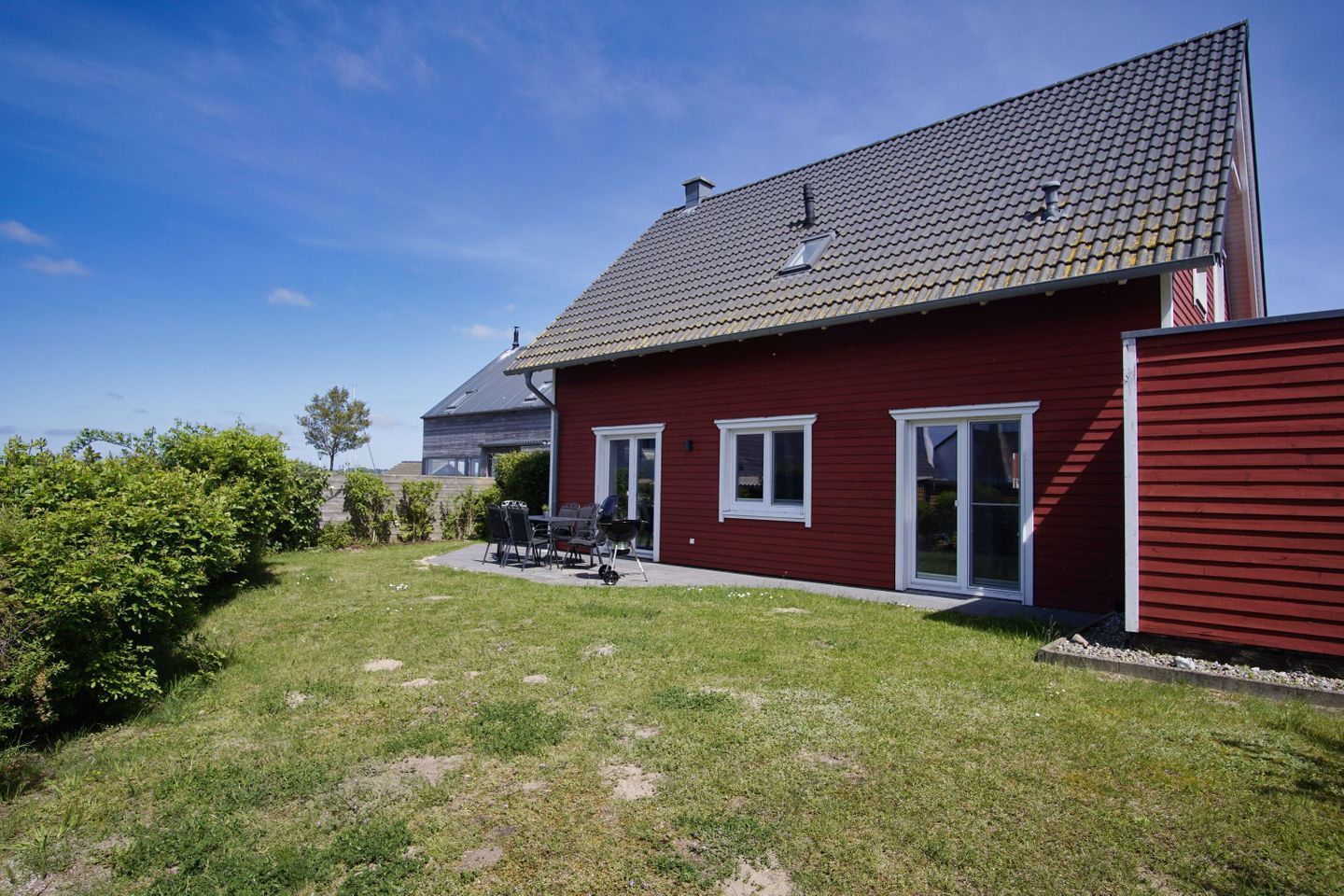 A red house with a sloped roof, a patio with outdoor furniture, and a well-maintained lawn.