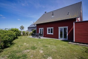 Una casa roja con techo inclinado, un patio con mobiliario exterior y un césped bien cuidado.