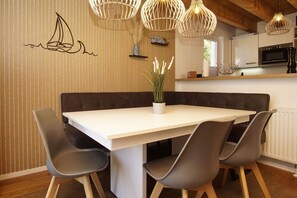 Un coin repas avec une table blanche, quatre chaises grises, un banc marron et une plante en pot.