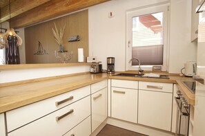A kitchen with wooden countertops, white cabinets, a built-in oven, a sink, and a window with blinds.