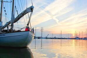 Un velero amarrado en un puerto deportivo, con aguas tranquilas y una puesta de sol al fondo.