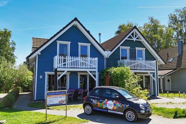 Une maison bleue à deux étages, avec un porche blanc et une voiture garée devant.