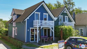 Ein zweistöckiges Gebäude mit einem Balkon, einer Veranda mit Stühlen und einem geparkten Auto davor.