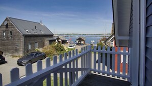 Ein Holzhaus mit Balkon, ein geparktes Auto davor und Blick auf Wasser und Boote.