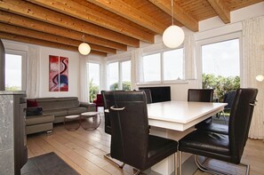 A modern living room with a sofa, a dining table with chairs, large windows, and a wooden ceiling. - Vacation home near the harbor with terrace and sea view - Ferienhaus TimpeTe Backbord - (Gager)