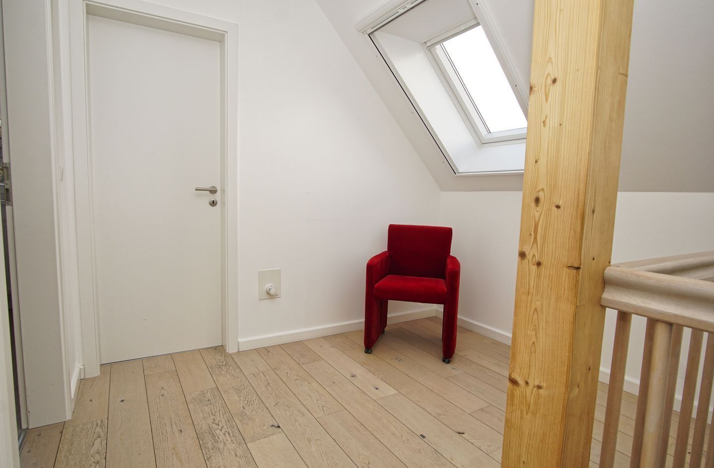 A room with a sloped ceiling, a red chair, and a wooden floor.