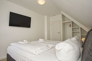 A bedroom with two beds, a TV mounted on the wall, and a closet with a sloped ceiling. - Vacation home near the harbor with a terrace and ocean view - Ferienhaus TimpeTe Backbord - (Gager)