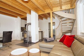 A modern interior with a wooden ceiling, a staircase, a sofa with red cushions, and a fireplace. - Vacation home near the harbor with terrace and sea view - Ferienhaus TimpeTe Backbord - (Gager)