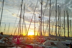 A marina with multiple sailboats docked, a sunset in the background, and a clear sky.