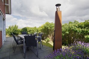 An outdoor patio with a table and chairs, a tall chimney, and surrounding greenery.