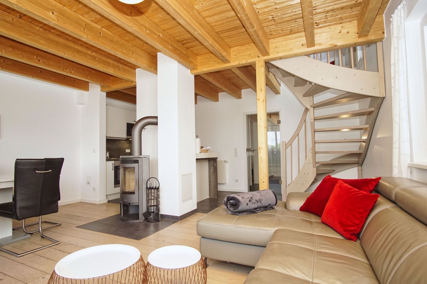 A modern interior with a wooden ceiling, a staircase, a sofa with red cushions, and a fireplace.