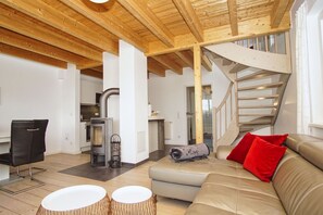 A modern interior with a wooden ceiling, a staircase, a sofa with red cushions, and a fireplace. - Vacation home near the harbor with a terrace and ocean view - Ferienhaus TimpeTe Backbord - (Gager)