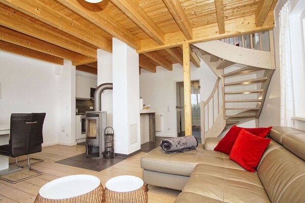 A modern interior with a wooden ceiling, a staircase, a sofa with red cushions, and a fireplace.