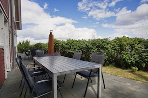 Eine Terrasse im Freien mit einem rechteckigen Tisch und vier Stühlen, umgeben von Pflanzen und einer Backsteinmauer.