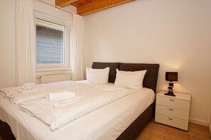 A neatly made bed with white linens and pillows, a bedside table with a lamp, and a window with closed blinds. - Vacation home close to the harbor with terrace and sea view - Holiday home TimpeTe Starboard (Gager)
