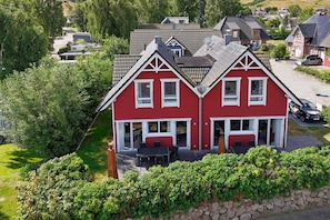 Ein rotes, zweistöckiges Haus mit Balkon, umgeben von Grünflächen und anderen Häusern.