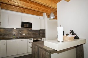 Eine moderne Küche mit weißen Schränken, einer Holzbalkendecke, einer Edelstahlspüle und einer Mikrowelle.