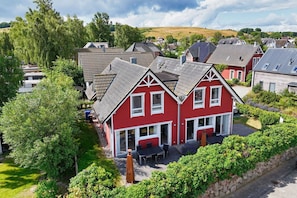 A red house with a sloped roof, a front porch, and a garden area with a table and chairs. - Vacation home near the harbor with a terrace and ocean view - TimpeTe Tribord Vacation Home (Gager)
