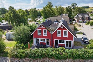 A red house with a gabled roof, a stone wall in front, and a clear view of the surrounding neighborhood.
