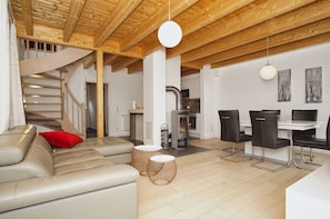 Ein modernes Wohnzimmer mit Sofa, Esstisch mit Stühlen, einer Treppe und einer Küchenzeile.