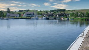 Un lago tranquilo con barcos, un muelle y casas al fondo.