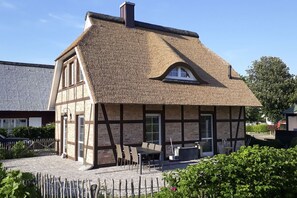 Ein traditionelles Fachwerkhäuschen mit Strohdach, einer kleinen Veranda und einer Steinsäule.