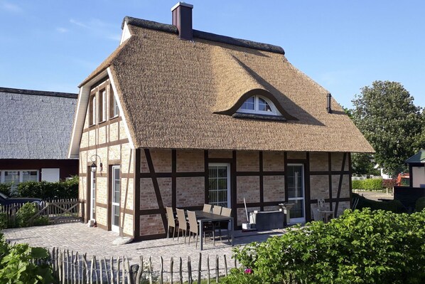 Ein traditionelles Fachwerkhäuschen mit Strohdach, einer kleinen Veranda und einer Steinsäule.