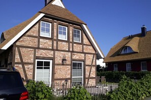 Ein traditionelles Fachwerkhäuschen mit einem steilen Dach, einem Schornstein und einem kleinen Garten mit Holzzaun und Grünpflanzen.