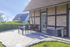 Ein Gebäude mit Ziegelverkleidung, einem Strohdach und einer Terrasse mit Gartenmöbeln.