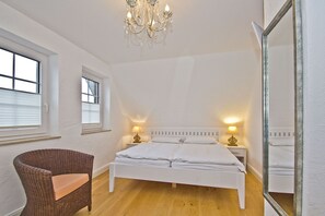 Ein Schlafzimmer mit einem großen Bett, zwei Nachttischlampen, einer Chandelieber, einem Sessel und einem Spiegel.