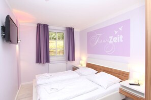 A bedroom with a bed, a TV mounted on the wall, a window with purple curtains, and a wall with the text "Fraumzeit". - Near the beach, vacation apartment with sauna and pool - Strandr.BaabeFeWo1.29 (Baabe)