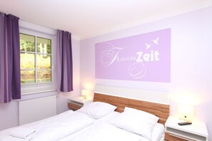 A bedroom with a bed, two bedside tables with lamps, a window with purple curtains, and a wall with the text "Traum Zeit". - Near the beach, vacation apartment with sauna and pool - Strandr.BaabeFeWo1.29 (Baabe)