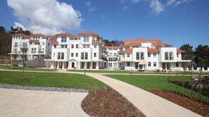 A large, multi-story building with a red-tiled roof, white exterior walls, and a paved walkway leading to the entrance. - Near the beach, vacation apartment with sauna and swimming pool - Strandr.BaabeFeWo1.29 (Baabe)