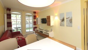 A room with a dining table, chairs, a sofa, a TV, and artwork on the wall. - Near the beach, vacation apartment with sauna and swimming pool - Strandr.BaabeFeWo1.29 (Baabe)
