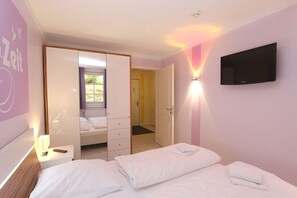 A bedroom with a bed, a bedside table with a lamp, a wardrobe, a TV mounted on the wall, and a door leading to another room. - Near the beach, vacation apartment with sauna and pool - Strandr.BaabeFeWo1.29 (Baabe)